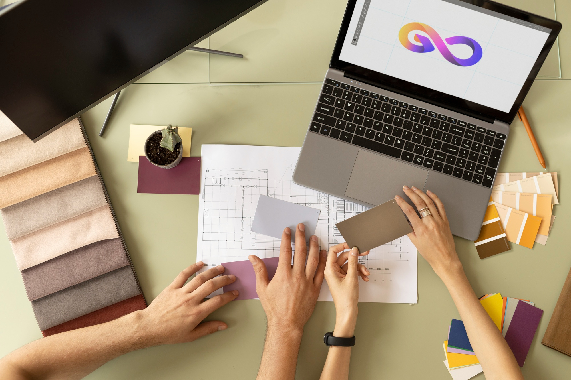 Hands of web designer and client selecting brand colors and design elements using swatches, sketches and laptop